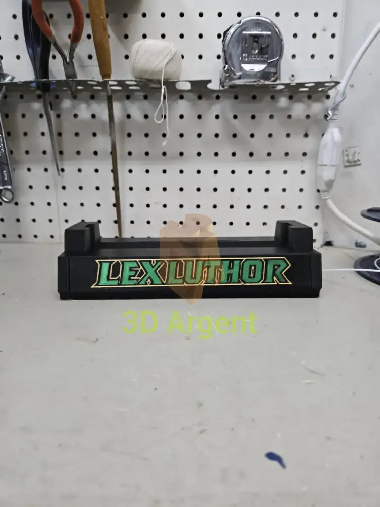 3D printed Lex Luthor comic slab display stand, black base with green and gold Lex Luthor text, photographed on a workbench