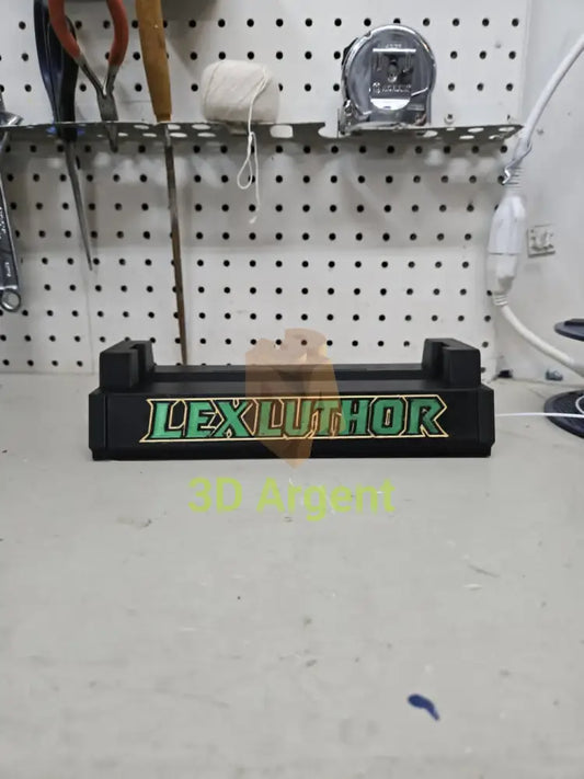 3D printed Lex Luthor comic slab display stand, black base with green and gold Lex Luthor text, photographed on a workbench