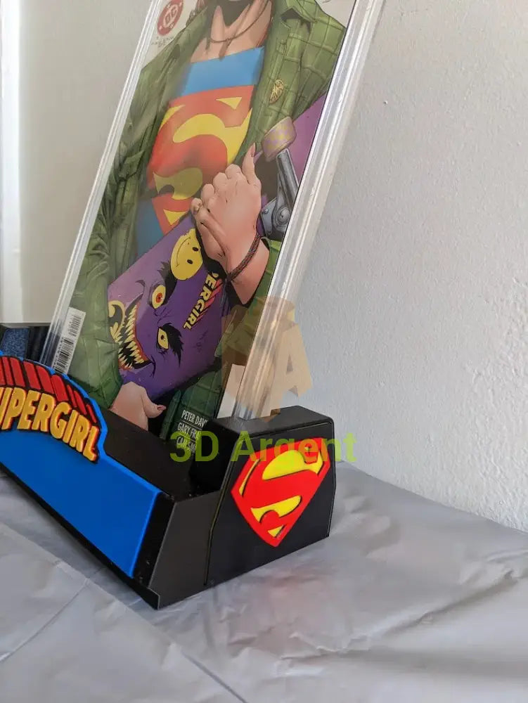 Close-up of the Supergirl comic display stand corner, showing the S-shield emblem and a graded comic slab held in the stand