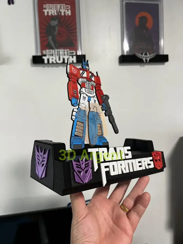 Transformers comic display stand held in hand, showing scale and Autobot and Decepticon emblems on the base